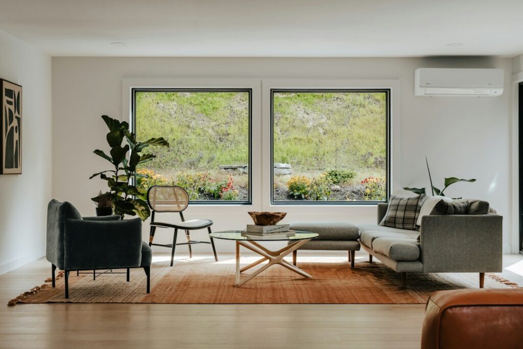A living room with large windows, seating and indoor plants